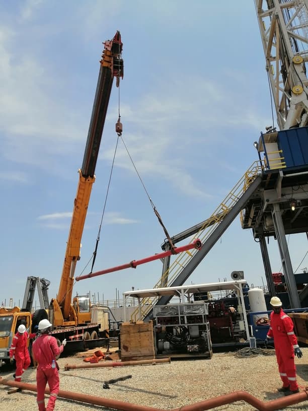 Crane lifting oilfield equipment beside a rig structure
