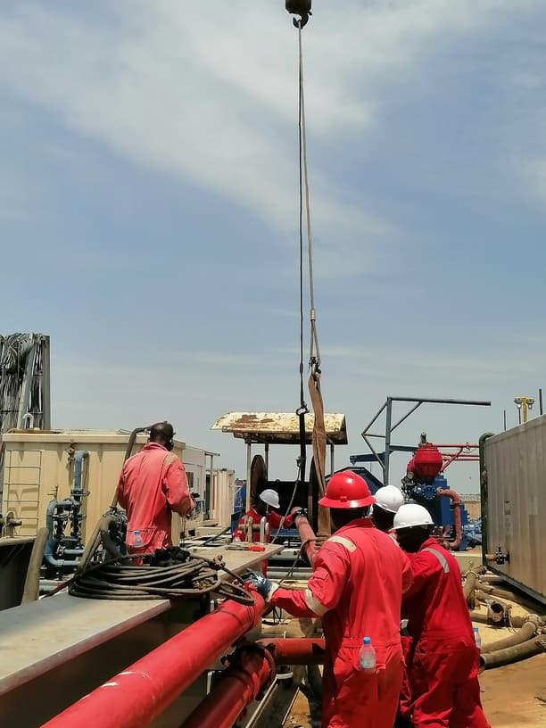 Field crew coordinating a lifted assembly near rig equipment