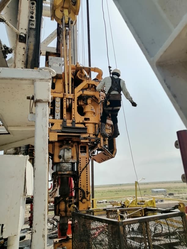 Oilfield worker climbing rig equipment with fall protection